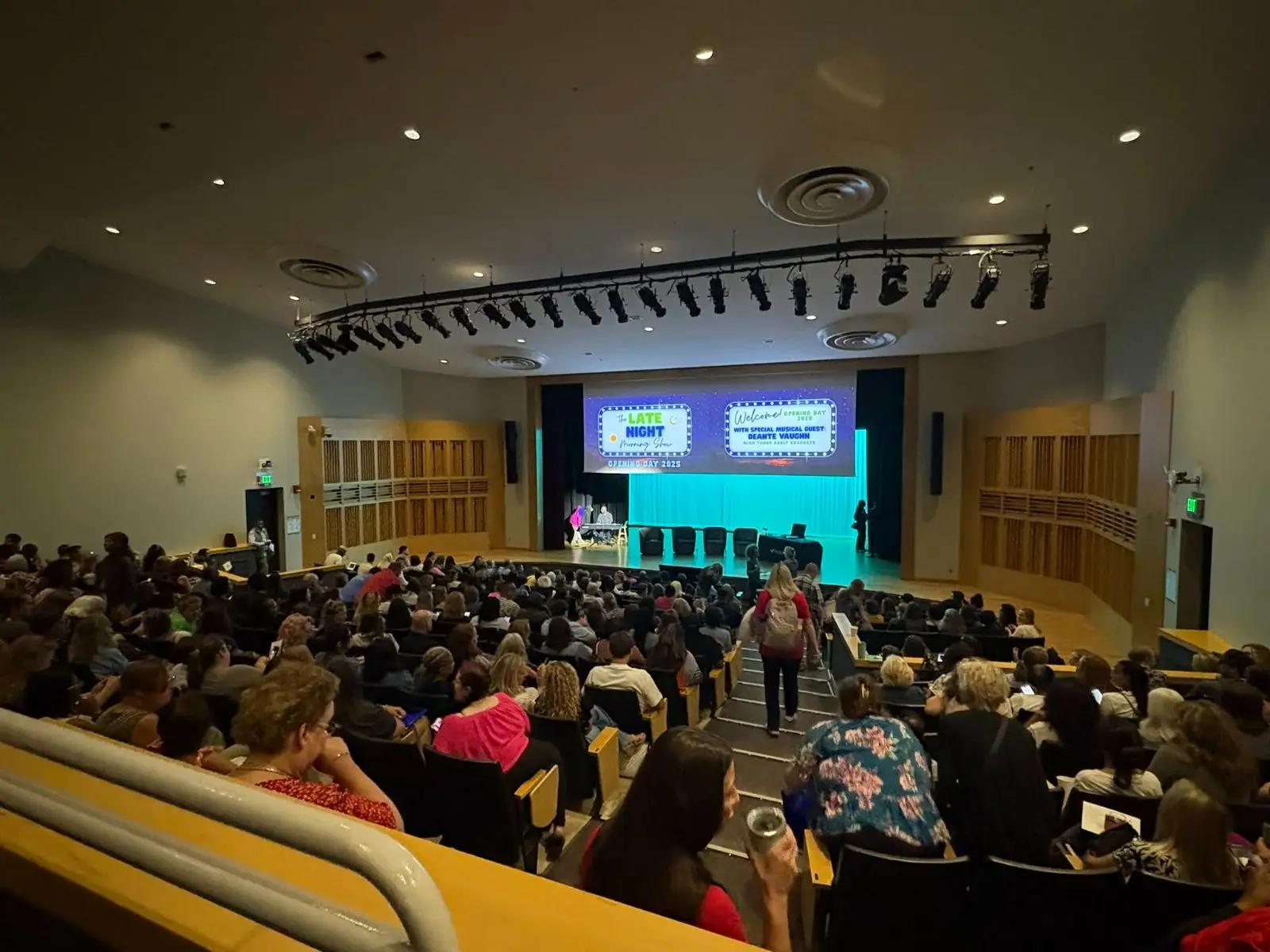 Packed auditorium facing a stage with a wide projection screen