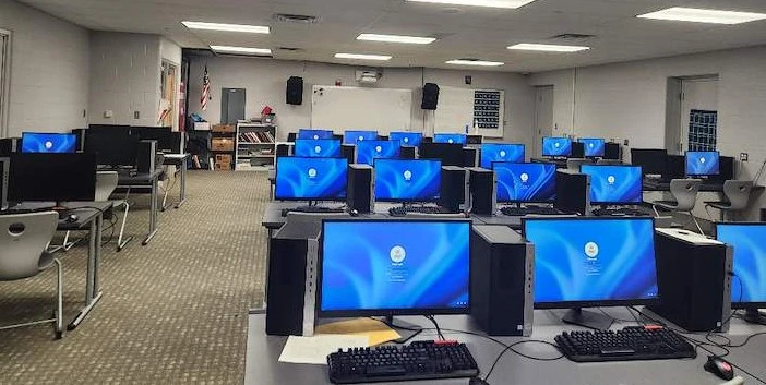 Computer lab classroom with rows of workstations and wall-mounted speakers