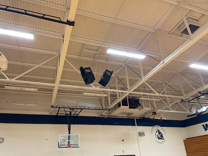Speaker clusters hung from the ceiling trusses of a school gymnasium