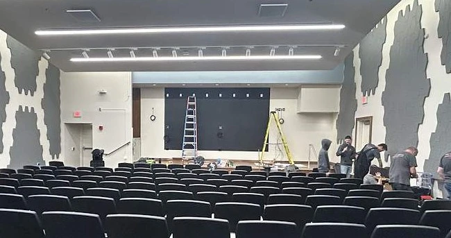Technicians on ladders installing a video wall at the front of a tiered lecture hall