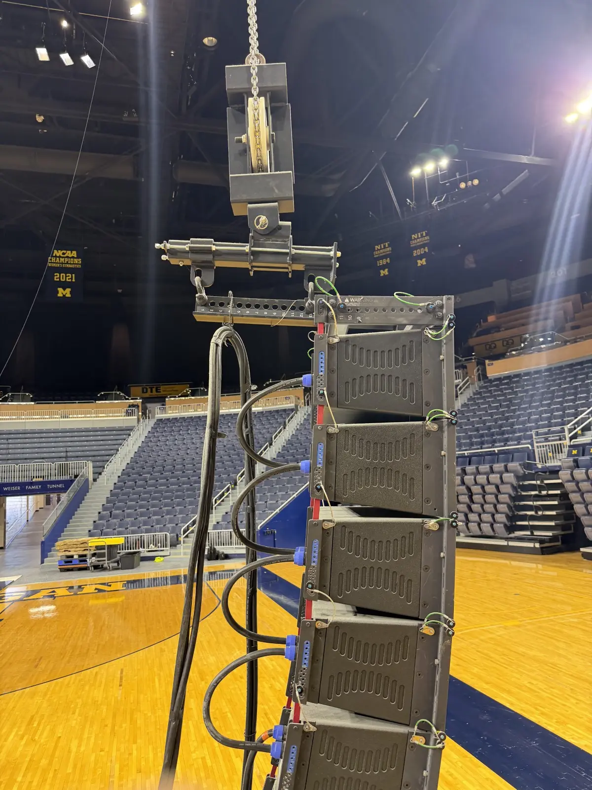 Side view of a speaker line array hanging from its rigging frame above an arena floor