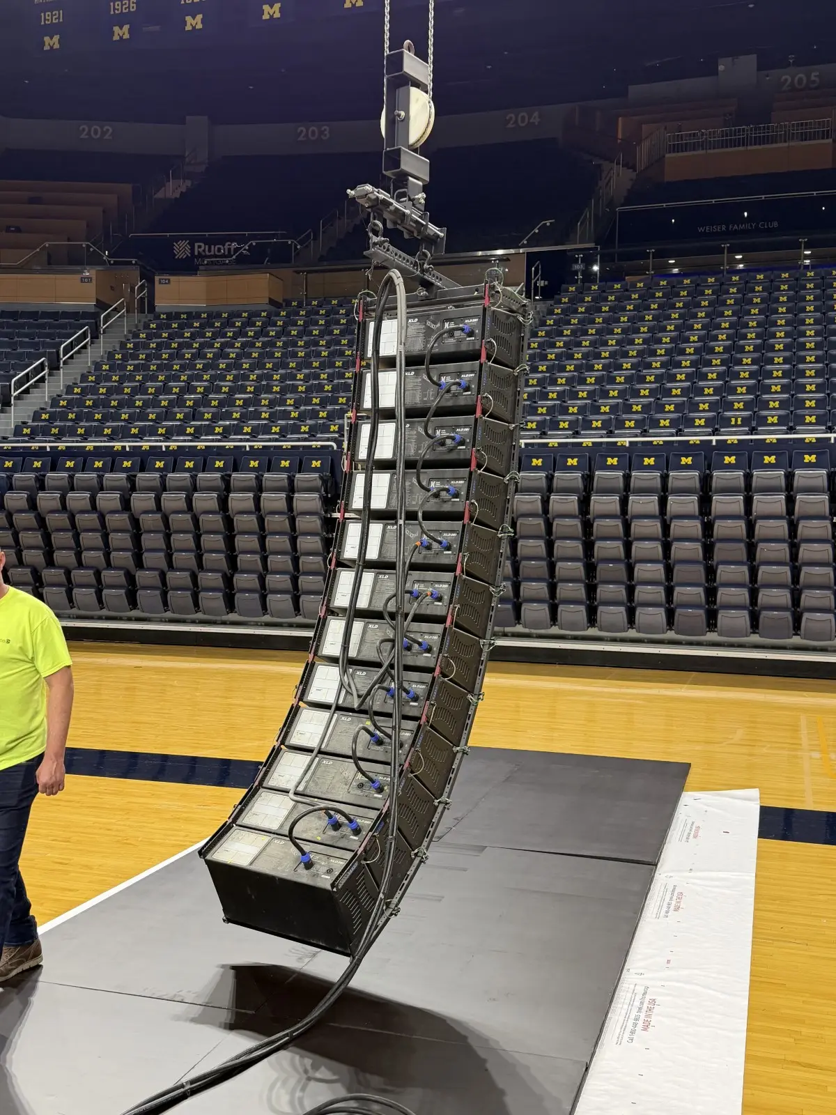 Curved line array of speakers being rigged above a basketball court in an empty arena